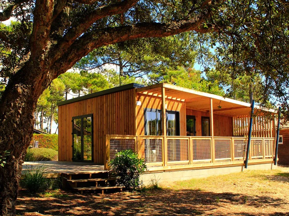Fotografía de un moderno chalet modular de madera en el camping La Marmotte en Ax-les-Thermes, enclavado en un pinar, con una gran terraza soleada